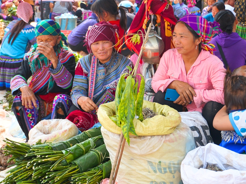 Femmes Hmong au marché de Bac Ha, partageant leur artisanat et produits locaux dans une ambiance authentique et colorée.