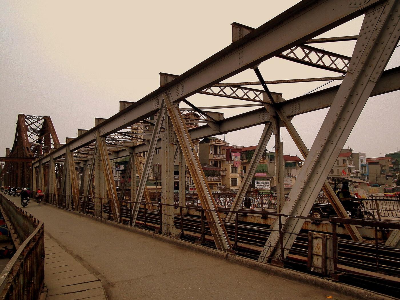 Traversée du Pont Long Biên à pied avec vue sur la structure en acier rivété et les maisons de Hanoi