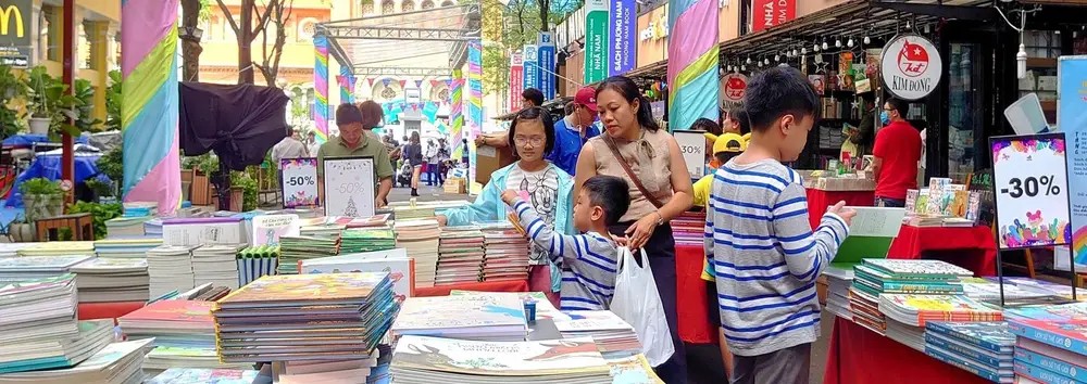 Famille et enfants choisissant des livres au coin lecture jeunesse de la rue du livre Nguyen Van Binh