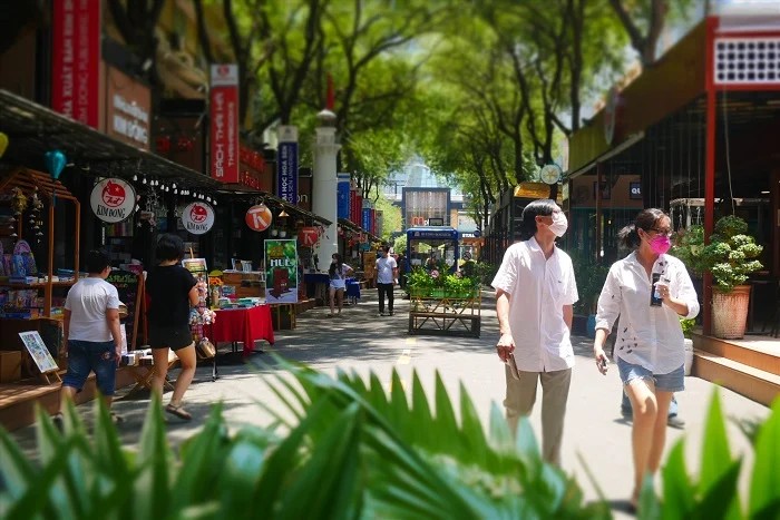 Promeneurs sur l'allée ombragée menant à la rue du livre Nguyen Van Binh