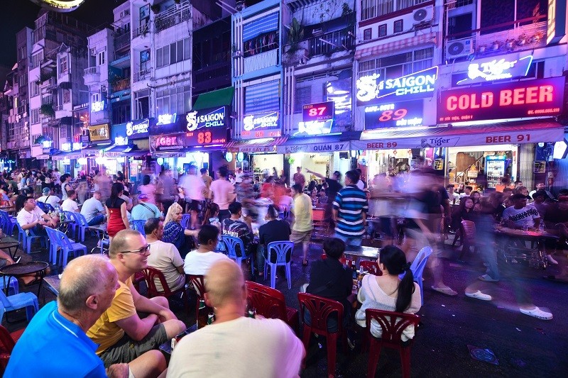 Touristes installés sur des tabourets pour déguster une bière de rue à Bui Vien