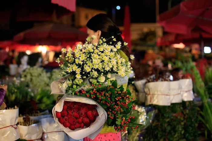 Marchande portant un assortiment de marguerites, roses et baies rouges au marché de nuit