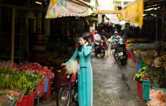Femme en áo dài bleu se promenant dans l'allée animée du marché de Ho Thi Ky