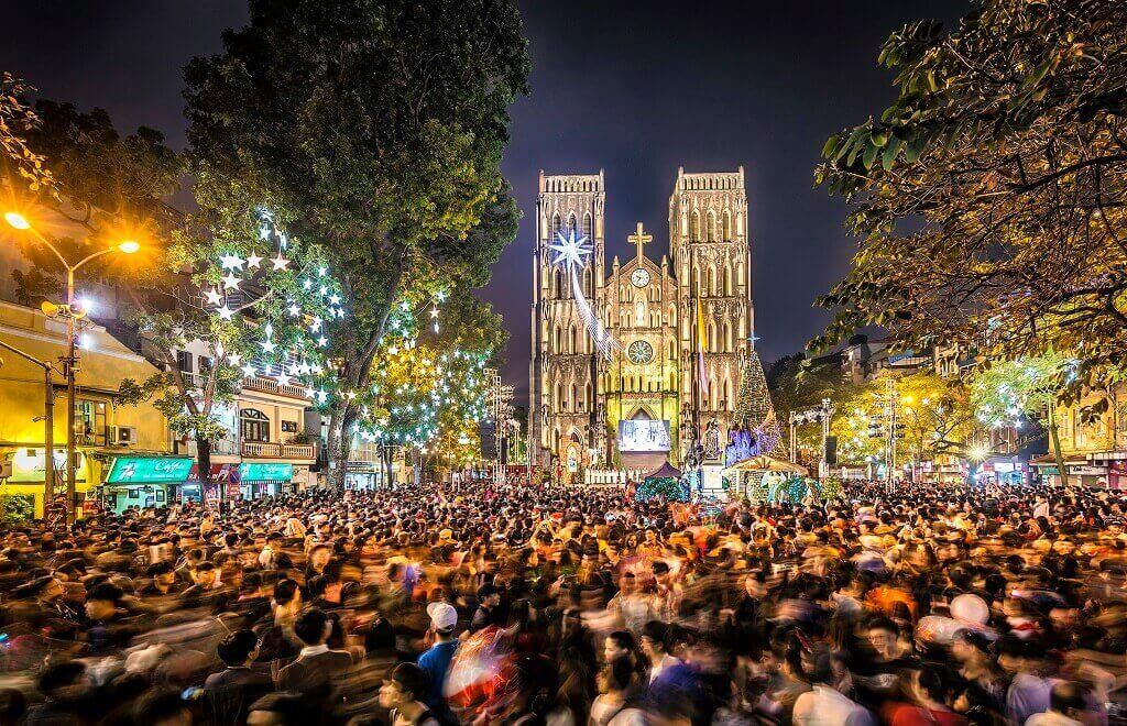 Foule rassemblée devant une cathédrale illuminée pour les fêtes de Noël au Vietnam