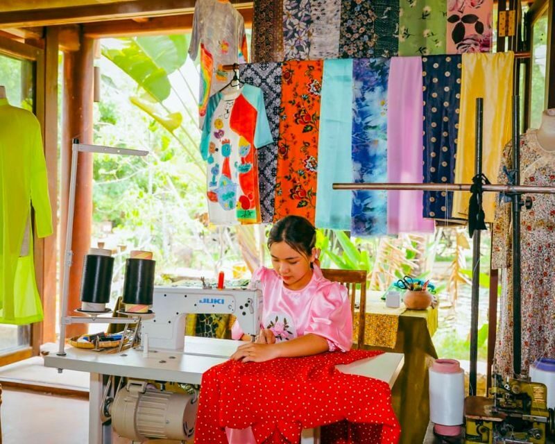 Couturière confectionnant un ao dai à la machine à coudre, entourée de tissus colorés, atelier du musée de l'Ao Dai
