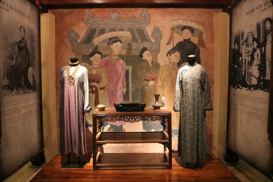 Costumes ao dai nam than à cinq pans exposés devant une fresque murale, datés d'environ 1884