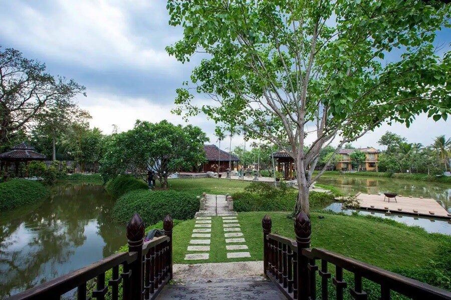 Pont en bois traditionnel menant aux pavillons du musée de l'Ao Dai, entourés d'un étang et d'un jardin verdoyant