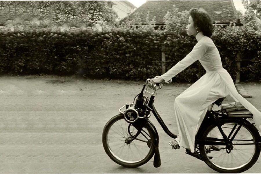 Photographie ancienne en noir et blanc d'une femme en ao dai blanc circulant à vélo dans les rues de Saigon