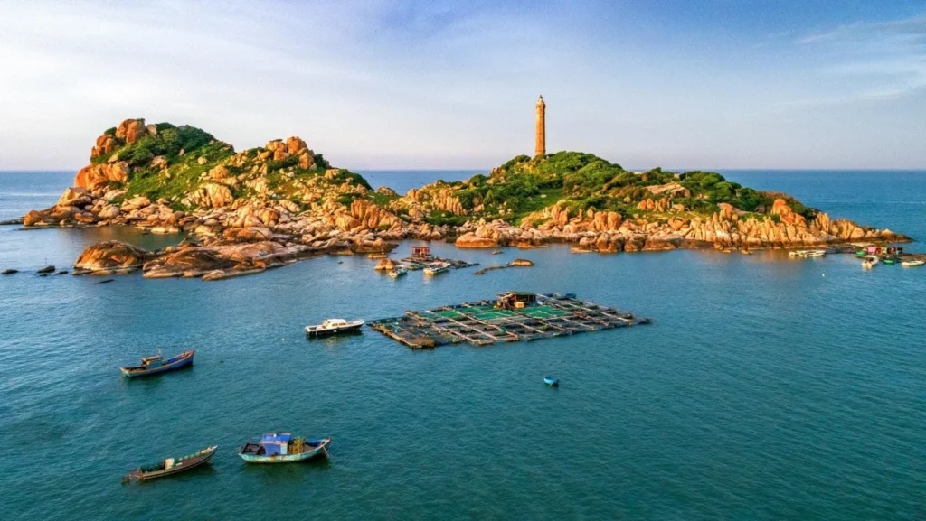 Vue depuis le large du cap et du phare de Ke Ga entourés de bateaux de pêche