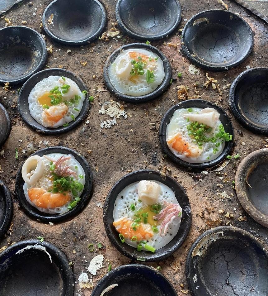 Banh can en cours de cuisson dans des moules en terre cuite
