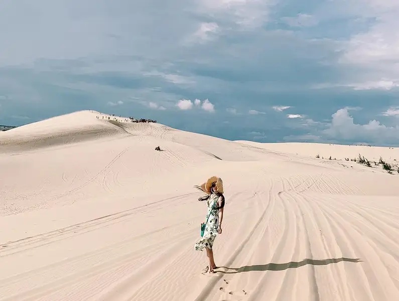 Une visiteuse en robe fleurie marchant sur les dunes blanches de Bau Trang
