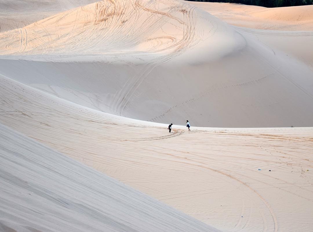 Deux visiteurs marchant sur les dunes blanches de Bau Trang au coucher du soleil