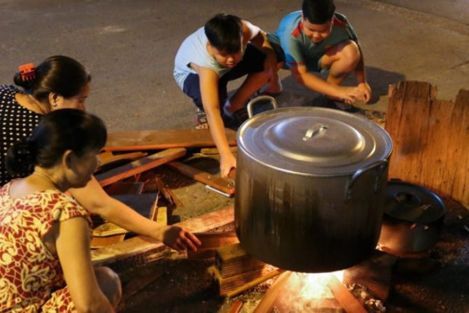 Une famille vietnamienne réunie autour du chaudron de banh chung pendant la nuit de cuisson