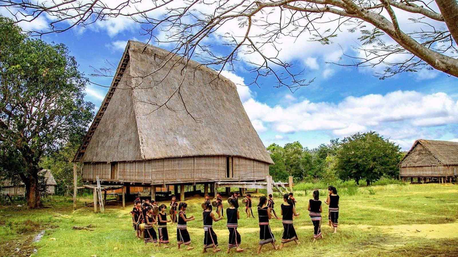 Danse traditionnelle de l’ethnie Bahnar en costumes noirs à rayures rouges devant un village à Kon Tum