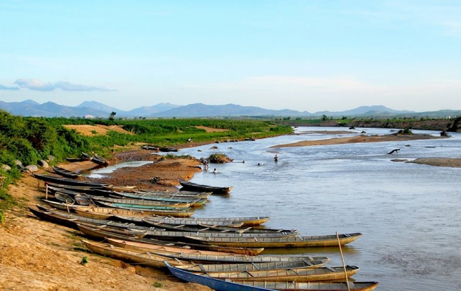 Pirogues en bois alignées sur la berge sableuse de la Đăk Bla avec baigneurs dans la rivière à Kon Tum