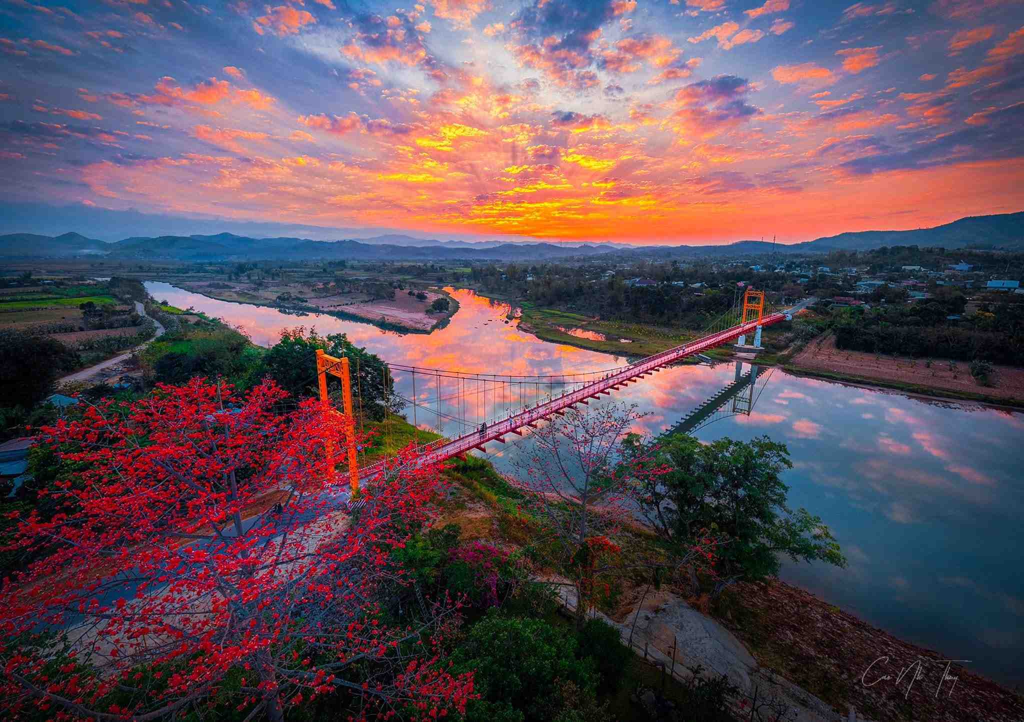 Vue plongeante sur le pont Kon Klor au coucher du soleil avec bombax en fleurs rouges au premier plan