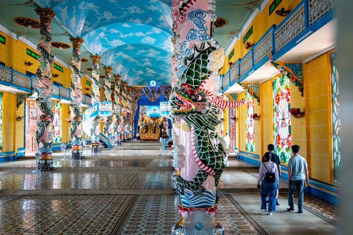 Visiteurs dans la nef du Temple Cao Dai entre les colonnes de dragons